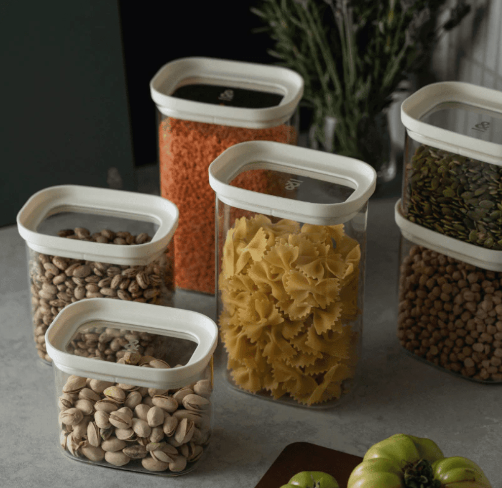 Seed & Sprout Tallow glass pantry containers with oatmeal-colored lids, neatly arranged on a countertop and filled with various dry foods.