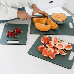 Seed & Sprout person slicing a rockmelon on a eucalyptus wood fibre chopping board in a bright kitchen, surrounded by freshly prepared citrus segments and radishes on matching boards.