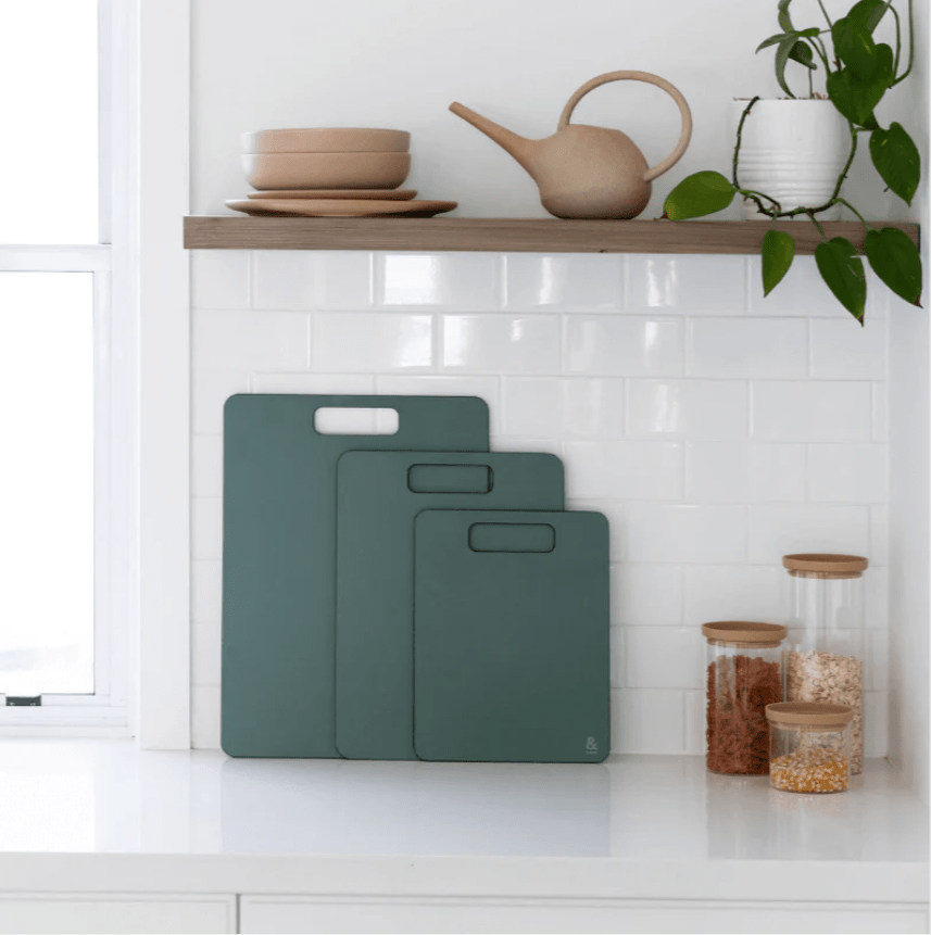 Seed & Sprout set of eucalyptus wood fibre chopping boards displayed in graduated sizes against a white tiled kitchen backsplash, alongside pantry jars and a styled shelf.