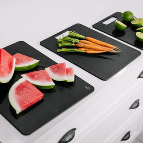 Seed & Sprout Liquorice wood fibre chopping boards arranged on a white kitchen counter, displaying fresh watermelon slices, whole carrots with green tops, and halved limes.