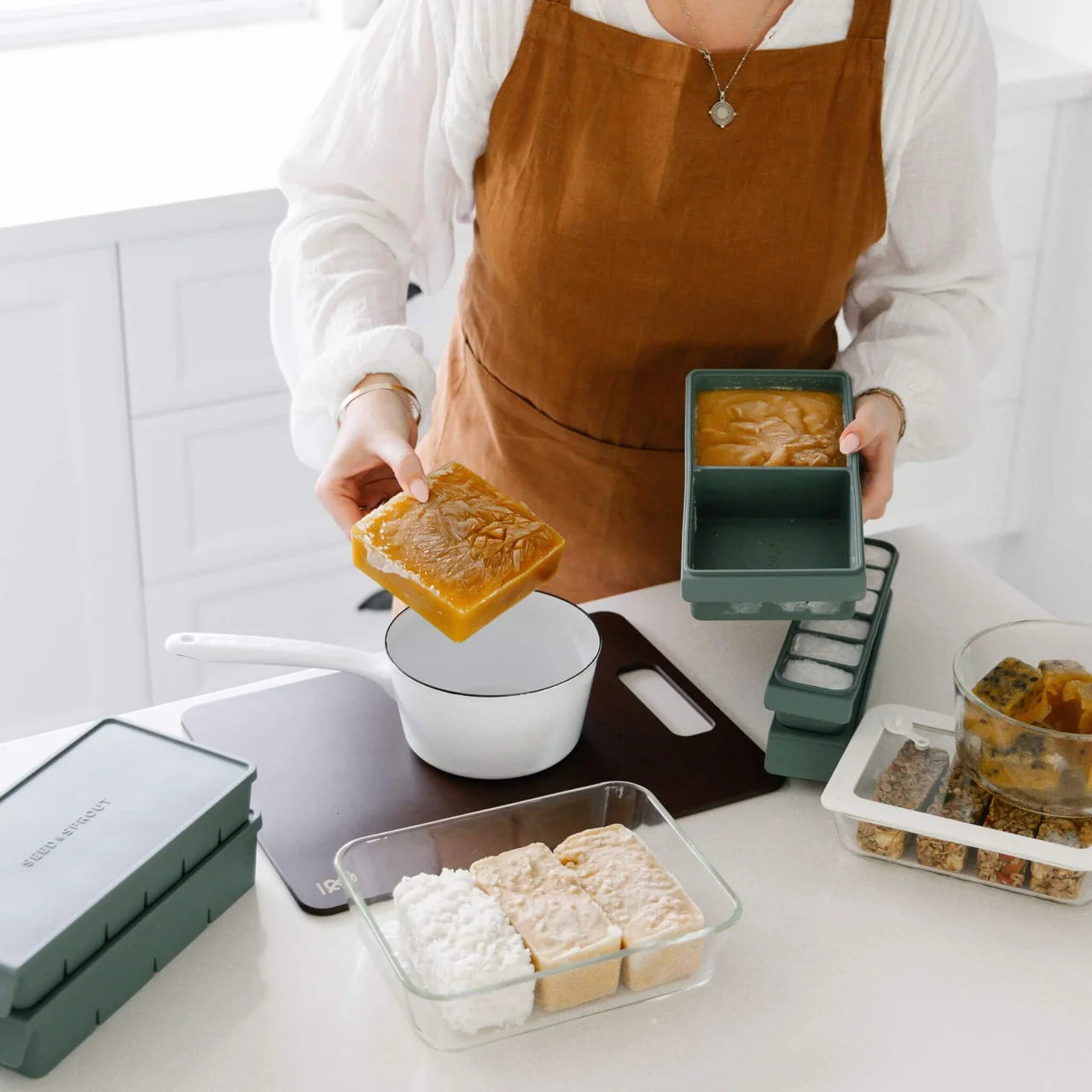 Seed & Sprout eucalyptus green silicone freezer trays being used to pop out frozen meal portions into a pot on a modern kitchen counter.