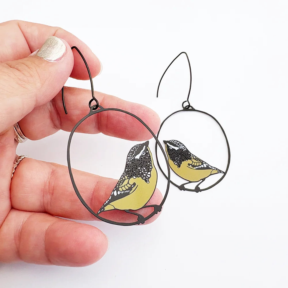 Hand holding DENZ Spotted Pardalote earrings on black wire frame.