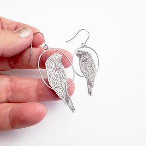 Hand holding DENZ Tawny Frogmouth earrings with hook fastening.