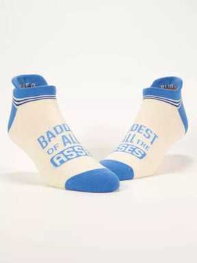 A pair of cream and blue Blue Q sneaker socks displayed standing upright featuring text reading "BADDEST OF ALL THE ASSES."