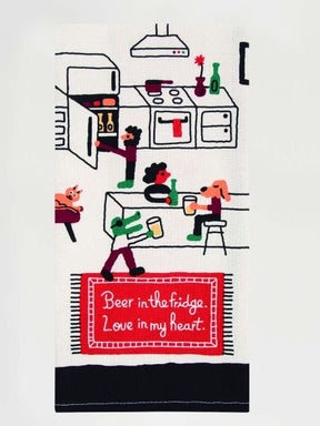 A folded white Blue Q tea towel illustrated with a lively kitchen scene and text on a red rug reading "Beer in the fridge. Love in my heart."