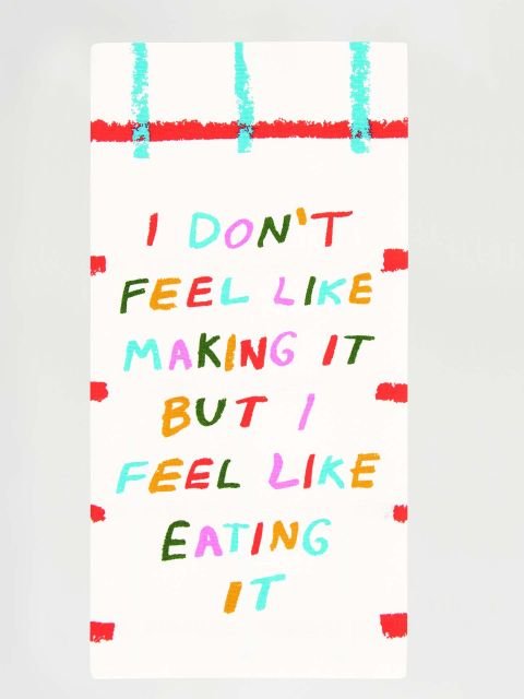 A white folded Blue Q tea towel with red and aqua grid lines, featuring colorful block letters reading "I DON'T FEEL LIKE MAKING IT BUT I FEEL LIKE EATING IT".