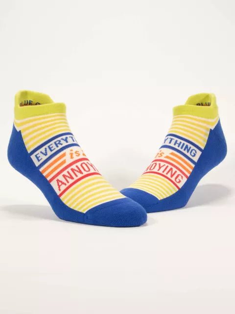 A pair of yellow-striped Blue Q ankle sneaker socks with royal blue accents reading "EVERYTHING is ANNOYING".