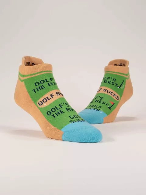 A pair of green and peach Blue Q ankle sneaker socks with light blue toes, featuring golf graphics and alternating text reading "GOLF'S THE BEST" and "GOLF SUCKS".