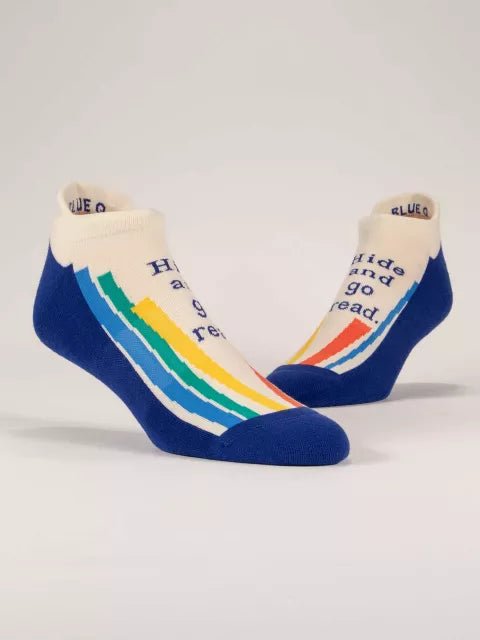 A pair of off-white Blue Q ankle sneaker socks with royal blue toes and heels, featuring colorful rainbow stripes and the text "Hide and go read."
