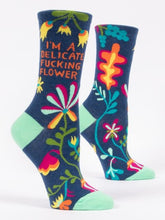 A pair of dark blue Blue Q women's crew socks covered in vibrant floral illustrations and orange text reading "I'M A DELICATE FUCKING FLOWER."