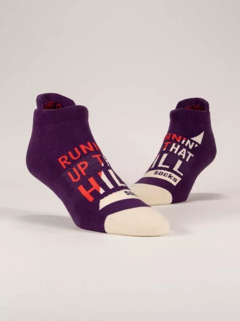 A pair of deep purple Blue Q ankle sneaker socks with off-white toes featuring bold red and white typography reading "RUNNIN' UP THAT HILL".