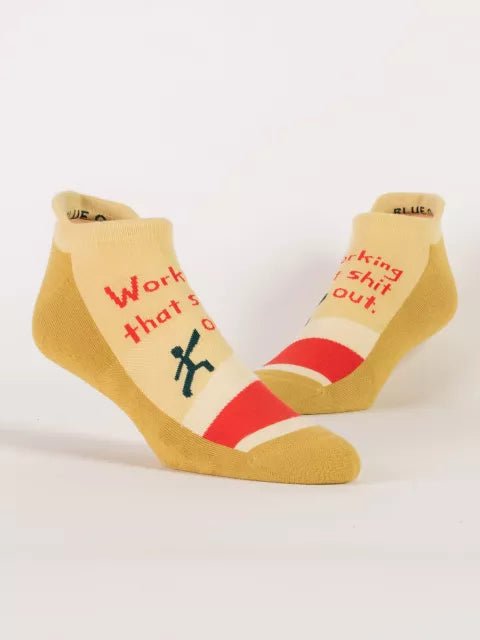 A pair of cream and golden-yellow Blue Q ankle sneaker socks featuring red text reading "Working that shit out."