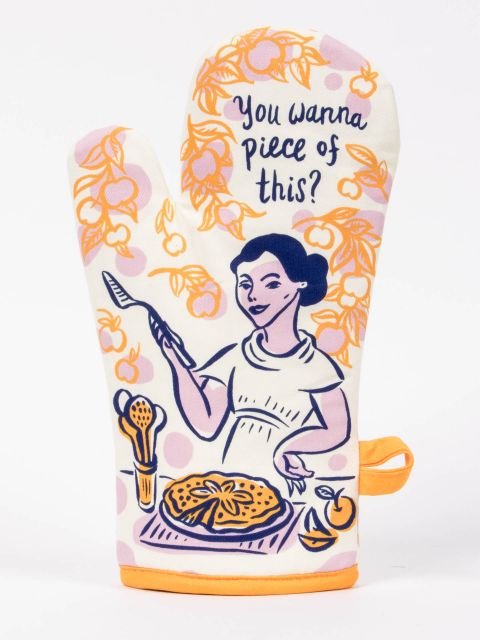 An off-white woven Blue Q oven mitt illustrated with a woman serving pie and text reading "You wanna piece of this?"