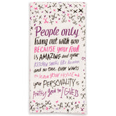 A white folded Blue Q tea towel printed with purple, pink, and black calligraphy stating "People only hang out with you because your food is AMAZING".