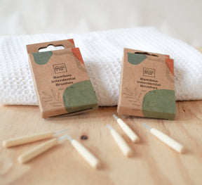 Brush It On bamboo interdental brush boxes and loose brushes displayed on a wooden surface in front of a white waffle towel