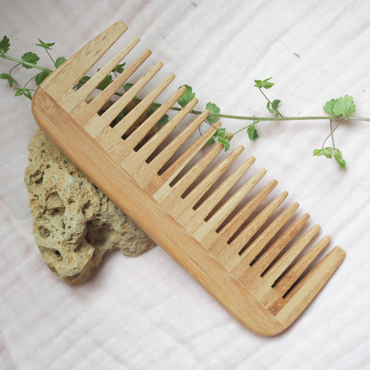 Brush It On bamboo wide tooth hair comb resting on a stone and light fabric with a leafy green vine
