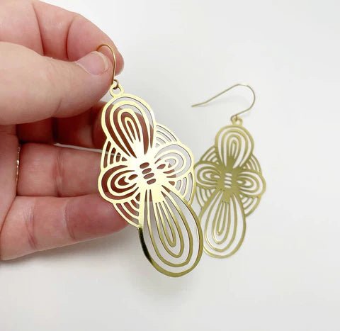 DENZ Bow dangles in gold, held by hand