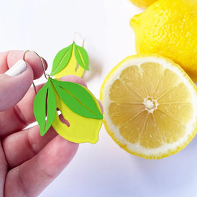 DENZ Lemon Dangles with green leaves held beside a sliced lemon.
