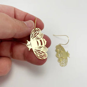 DENZ Mini Bee dangles in gold, held by hand