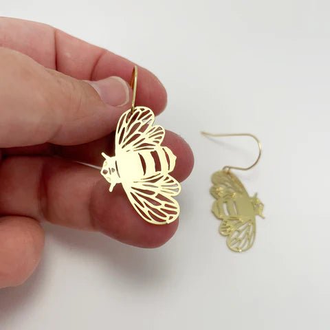 DENZ Mini Bee dangles in gold, held by hand