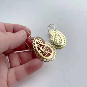 DENZ Mini Paisley dangles in gold, held by hand