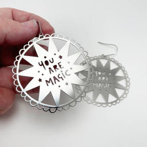 DENZ You Are Magic in silver earrings, held by hand