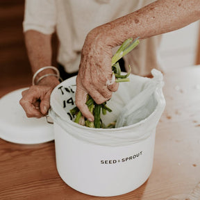 Seed & Sprout off-white mushroom compost bin lined with a compostable bag on a wooden table with the lid beside it.