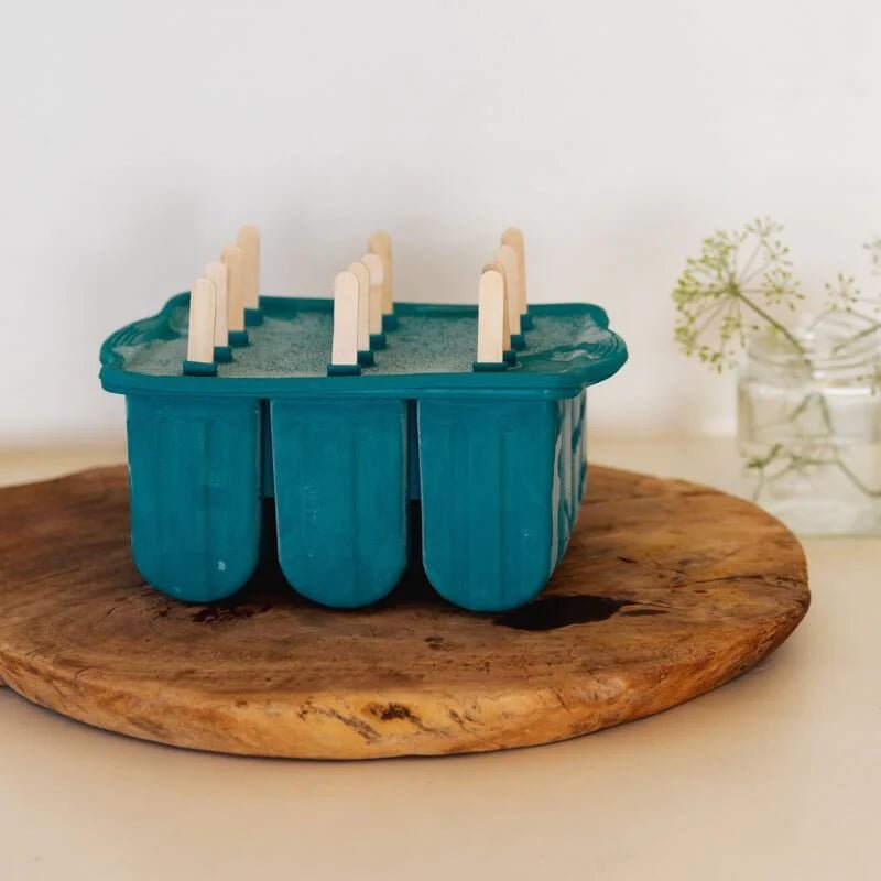 Seed & Sprout juniper silicone icy pole mould filled with liquid ready for freezing, resting on a round wooden cutting board.