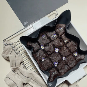 Seed & Sprout graphite square silicone un-baking paper holding baked brownies decorated with edible flowers in a white baking dish on an oven rack.