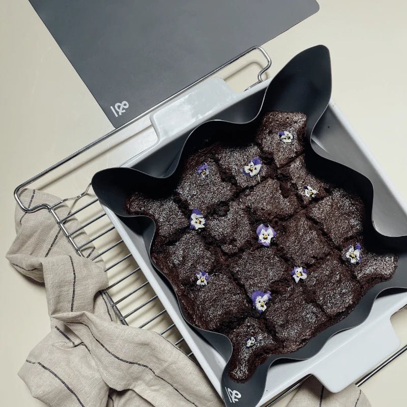 Seed & Sprout graphite square silicone un-baking paper holding baked brownies decorated with edible flowers in a white baking dish on an oven rack.